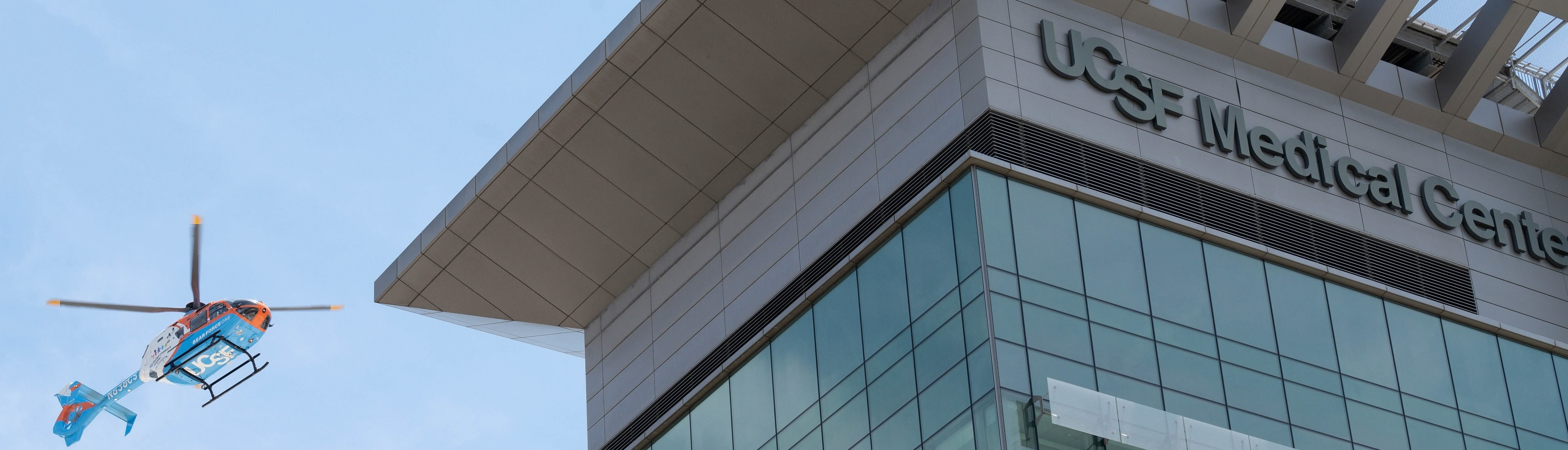 Helicopter approaching the UCSF Medical Center rooftop against a clear sky